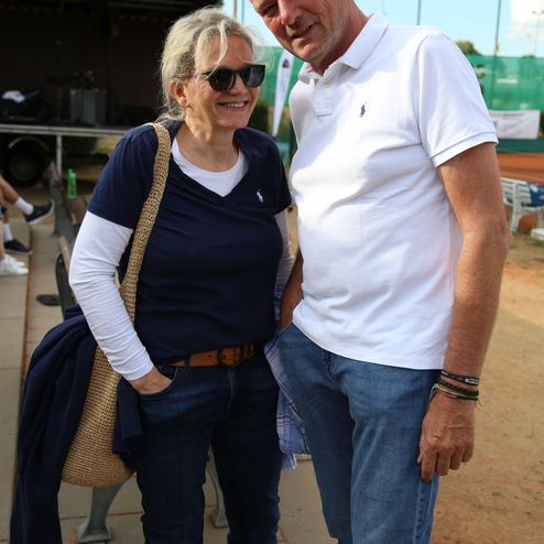 Ein Mann und eine Frau stehen gemeinsam, beide l&auml;cheln, in sportlicher Freizeitkleidung auf einem Au&szlig;enplatz.