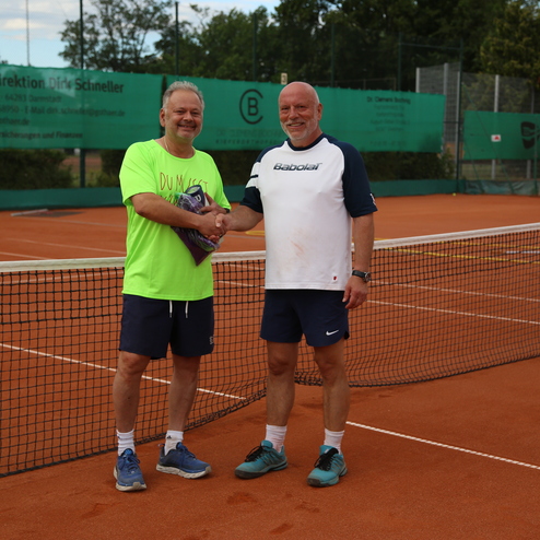 Zwei M&auml;nner sch&uuml;tteln sich die H&auml;nde auf einem Tennisplatz mit orangefarbener Spielfl&auml;che im Hintergrund.