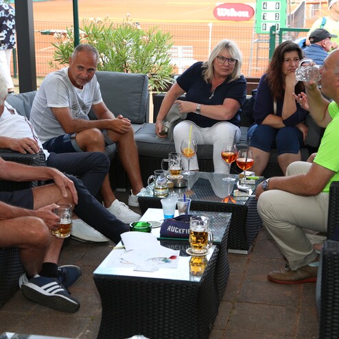 Gruppe von sieben Personen sitzt entspannt in einer Lounge, trinkt Getr&auml;nke und unterh&auml;lt sich in einer sportlichen Umgebung.