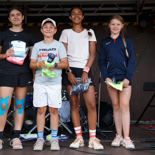 Vier Kinder stehen auf einer B&uuml;hne, jeder mit Sportkleidung und pr&auml;miierten Gegenst&auml;nden in den H&auml;nden.