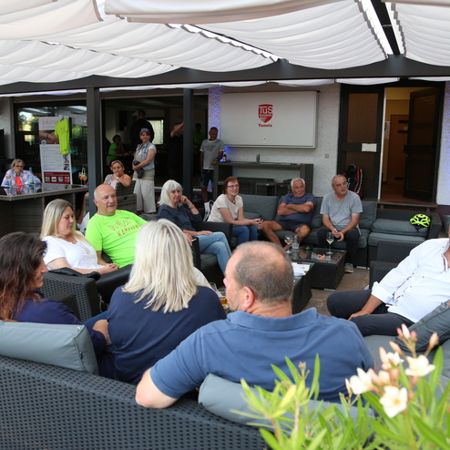 Gruppe von Menschen sitzt entspannt in einem Au&szlig;ensalon, umgeben von Pflanzen und einem modernen Ambiente.
