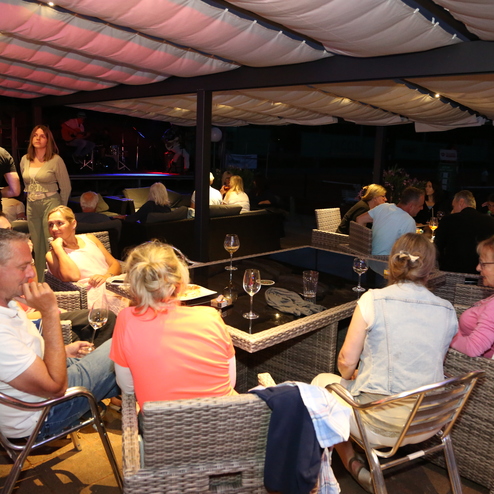 Gesellige Runde in einem Lounge-Bereich mit G&auml;sten, die an Tischen sitzen und Getr&auml;nke genie&szlig;en. Abendliche Atmosph&auml;re.