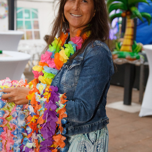 Frau mit bl&uuml;hender Sommerkleidung und buntem Blumenkranz in einer festlichen Umgebung mit Palmen-Dekoration.