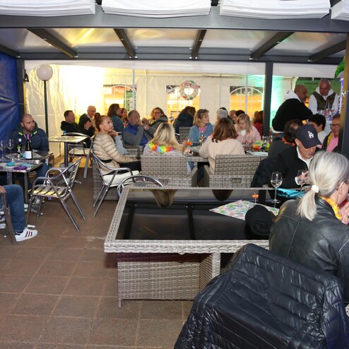 Menschen sitzen an Tischen in einem festlich dekorierten Innenraum mit bunten Lichtern und Palmen.