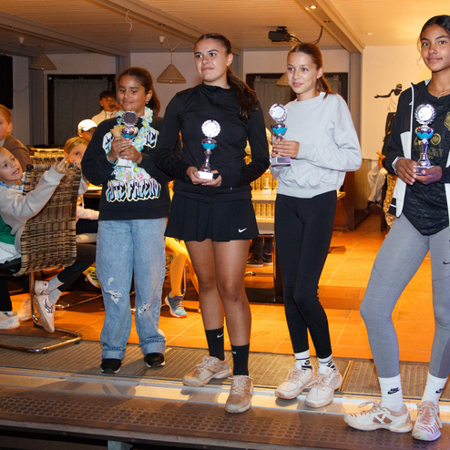 Vier M&auml;dchen stehen im Vordergrund, halten Pokale. Im Hintergrund sitzen weitere Kinder in einem Gastraum.