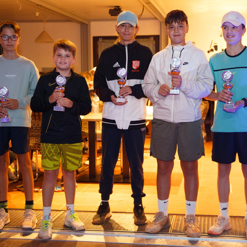 F&uuml;nf Jugendliche stehen mit Pokalen vor einer Fensterfront in einem Festsaal. Alle tragen sportliche Kleidung und l&auml;cheln.