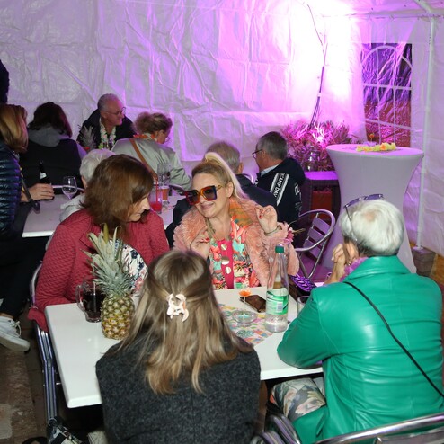 Gruppe von Personen sitzt an einem Tisch in einem Zelt, umgeben von dekorativem Licht und Getr&auml;nken.