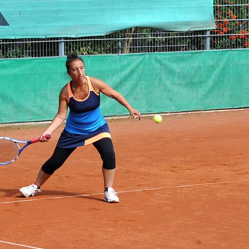 Tennisspielerin in Bewegung, schlägt einen Ball auf einem roten Sandplatz, umgeben von grünen Wänden.