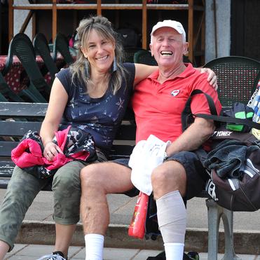 Ein lächelndes Paar sitzt auf einer Bank, umgeben von Tischtennisausrüstung und grünen Stühlen.