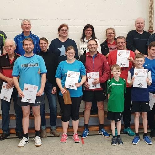 Gruppe von Tischtennisspielern mit Urkunden in einer Sporthalle, stehend auf einer Bank.