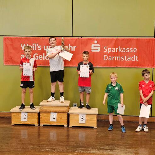 Fünf Kinder stehen auf Treppchen und halten Urkunden in einer Sporthalle, mit Banner von Sparkasse Darmstadt im Hintergrund.