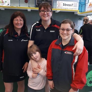 Vier Personen posieren in Sportkleidung für ein Foto in einer Tischtennishalle, darunter ein kleines Mädchen.