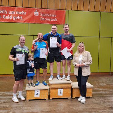 Vier Tischtennisspieler und ein Kind stehen auf einem Podium, während eine Frau daneben steht. Alle halten Urkunden.