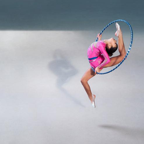 Sportlerin in pinkem Outfit vollbringt einen akrobatischen Sprung durch einen Mädchen-Hoop-Ring auf grauem Boden.