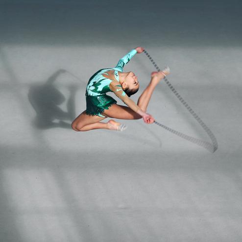 Junge Kunstturnerin in einem grünen Leotard springt und schwingt ein Seil auf einem grauen Boden.