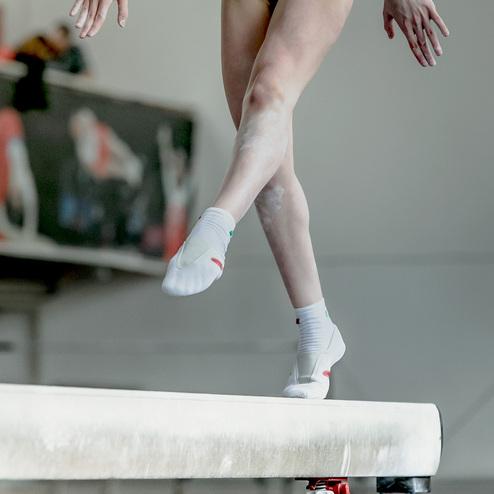 Nahaufnahme eines Gymnasten, der auf einem Schwebebalken steht, mit einem fokussierten Fuß und gespannten Beinen.