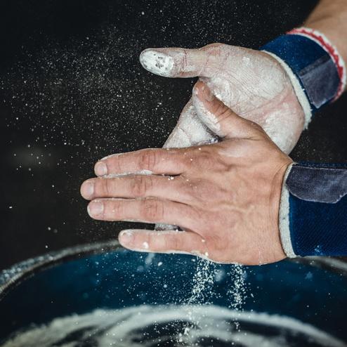 Hände mit Chalkpulver in Aktion, während sie über einen blauen Behälter mit weiterem Chalkpulver reiben.