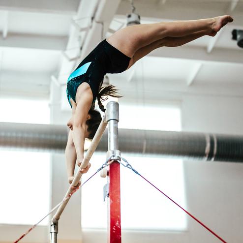 Turnerin führt einen Schwung an den Parallelbarren in einer Sporthalle durch.