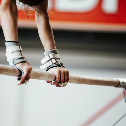 Nahaufnahme von Händen, die an einem Turngerät mit Gurtgriffen den Holzstangen halten.