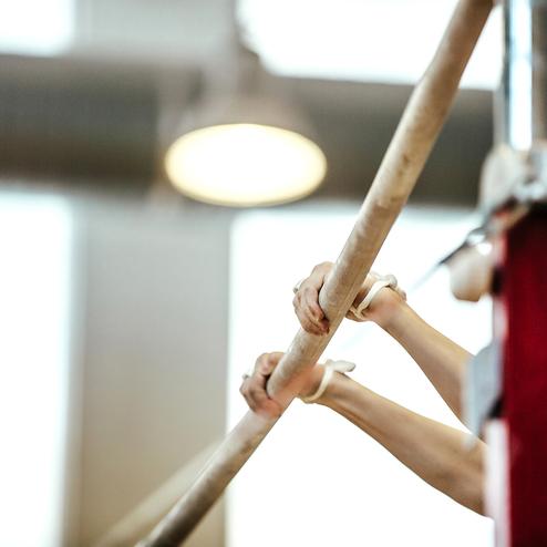 Hände einer Körperturnerin, die einen Schwebebalken mit Handgriffen aus Holz halten. Hintergrund unscharf.