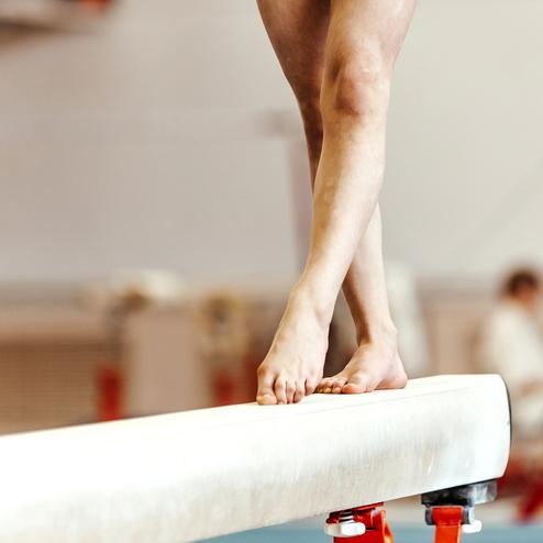 Eine Athletin balanciert barfuß auf einem Schwebebalken in einem Turnstudio.