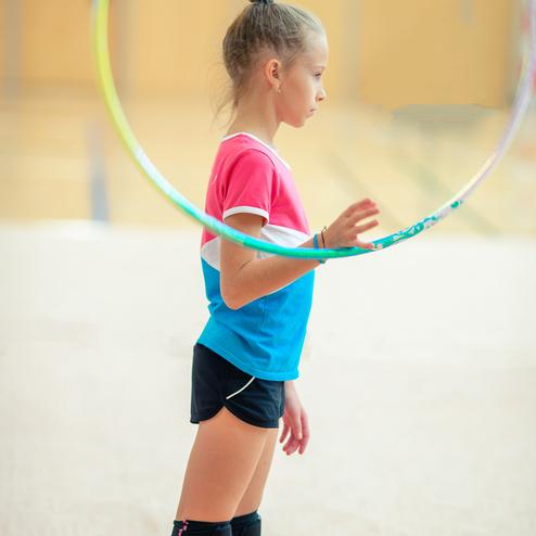 Mädchen mit einem bunten Shirt steht seitlich, während sie einen Hula-Hoop-Reifen in der Hand hält.