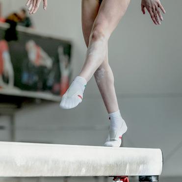 Nahaufnahme eines Gymnasten, der auf einem Schwebebalken steht, mit einem fokussierten Fuß und gespannten Beinen.