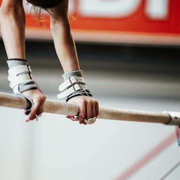 Nahaufnahme von Händen, die an einem Turngerät mit Gurtgriffen den Holzstangen halten.