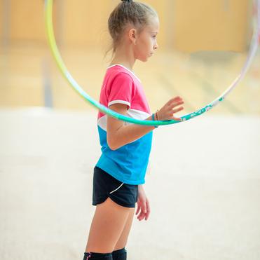 Mädchen mit einem bunten Shirt steht seitlich, während sie einen Hula-Hoop-Reifen in der Hand hält.