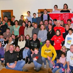 Gruppenfoto von etwa 60 Personen in einem Aufenthaltsraum, senioren und kinder stehen und sitzen eng beieinander.