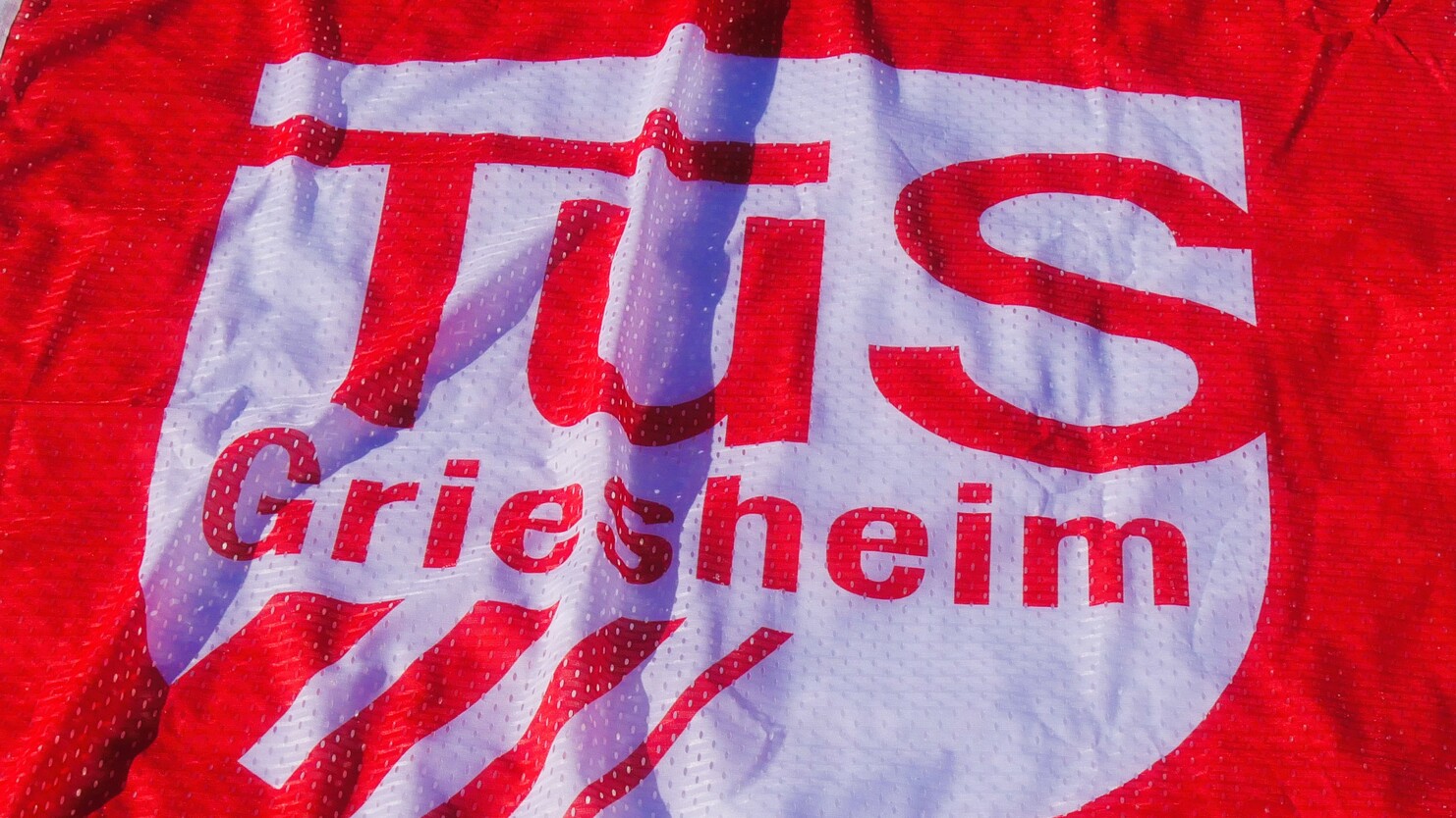 Logo der TuS Griesheim auf einem roten Stoffbanner, teilweise gefaltet und leicht zerknittert.