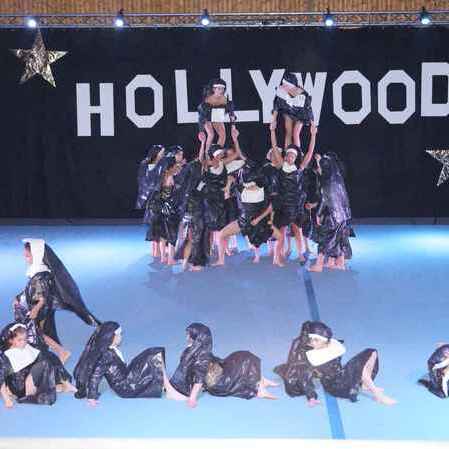 Gruppe von Tänzern in schwarzen Kostümen auf einer Bühne mit dem Schriftzug "HOLLYWOOD" im Hintergrund.