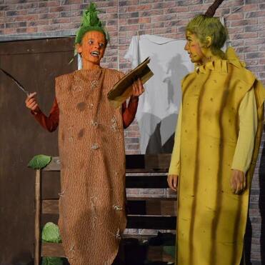 Zwei Personen in Kostümen als Karotte und Banane stehen auf einer Bühne, im Hintergrund eine Backsteinmauer.