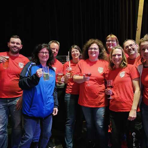 Gruppe von Menschen in roten T-Shirts, die mit Getr&auml;nken ansto&szlig;en, vor einem dunklen Hintergrund.