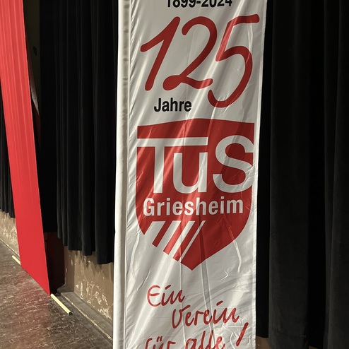 Banner mit dem Aufdruck &bdquo;125 Jahre TuS Griesheim 1899-2024 &ndash; Ein Verein f&uuml;r alle!&ldquo; vor schwarzem Vorhang.