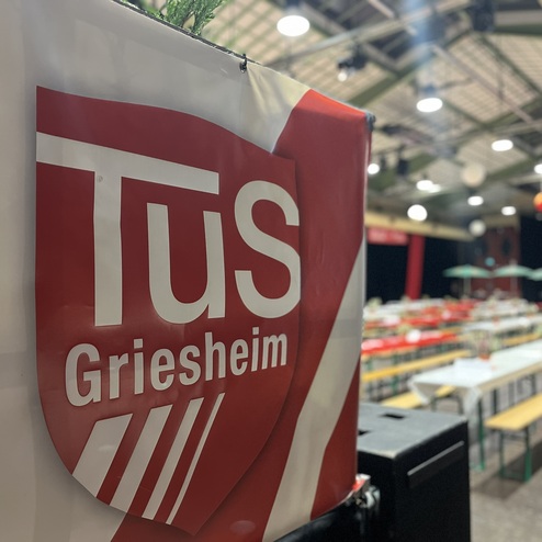 Logo der TuS Griesheim an einer Wand, mit Blick auf einen festlich dekorierten Veranstaltungsraum.