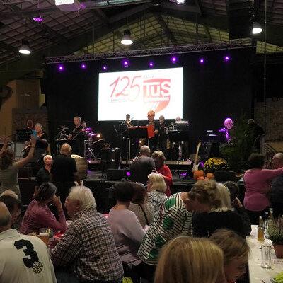 Feierliche Veranstaltung mit Liveband auf einer B&uuml;hne, Menschen tanzen und genie&szlig;en die Feierlichkeit in einer festlichen Atmosph&auml;re.