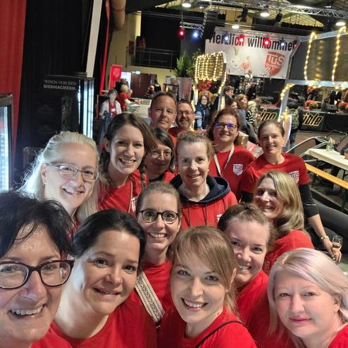 Gruppe von Personen in roten T-Shirts mit dem Logo der TUS Griesheim, lächelnd im Innenraum einer Veranstaltung.