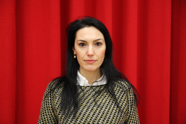 Porträt einer Frau mit schwarzem Haar, in einem gestreiften Oberteil, vor einem roten Hintergrund.