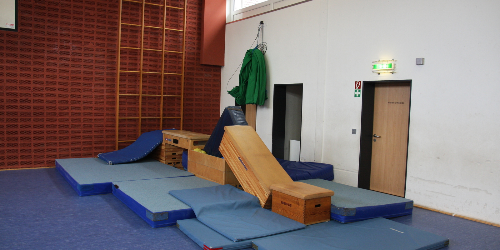 Kletterger&uuml;st aus Matten und Holzkisten in einer Turnhalle mit blauen Matten und einer Kletterwand im Hintergrund.