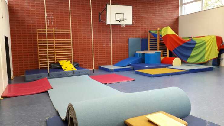 Bewegungsraum mit verschiedenen Turngeräten, Matten, einem Basketballkorb und buntem Spielmaterial.