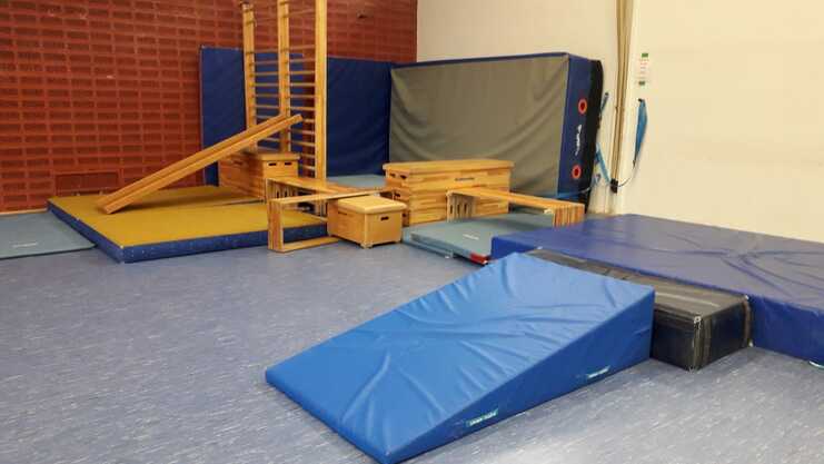 Kletter- und Turnbereich mit Holzgeräten, Matten und einer schrägen Plattform in einem Gymnastikraum.