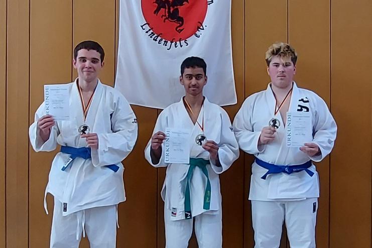 Drei Judoka in weißen Anzügen halten Medaillen und Urkunden vor einem Banner des Judoclubs Nibelungen Lindenfels.