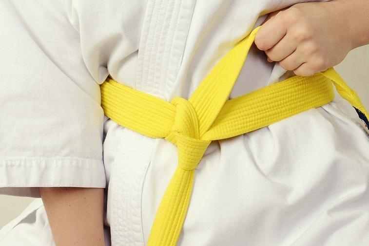 Nahaufnahme eines Kindes im weißen Karateanzug, das einen gelben Gürtel bindet.