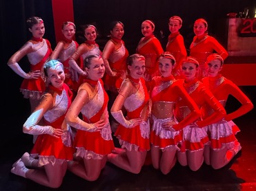 Gruppe von Tänzerinnen in roten Kostümen posiert auf der Bühne vor dem Banner „TuS Total“.