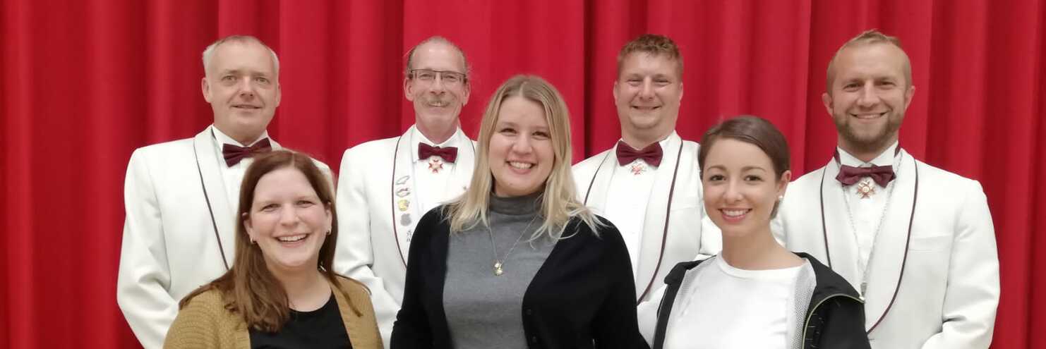 Gruppenfoto von sechs Personen vor rotem Vorhang, einige in Anzügen und Fliegen, andere in Freizeitkleidung.