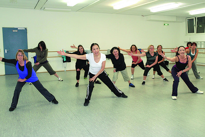 Gruppe von Frauen in sportlicher Kleidung, die synchron in einem Tanzstudio tanzen.