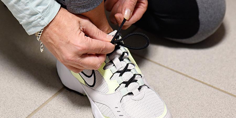 Nahaufnahme einer Person, die die Schn&uuml;rsenkel eines wei&szlig;en Sportschuhs mit schwarzer Schn&uuml;rung bindet.