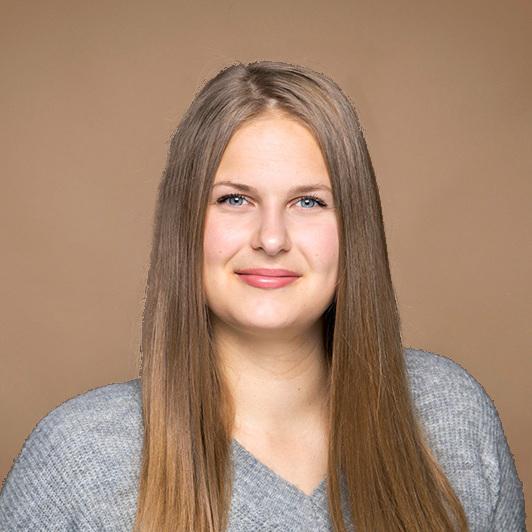 Porträt einer lächelnden Frau mit langen, glatten Haaren in grauem Pullover vor einem neutralen Hintergrund.