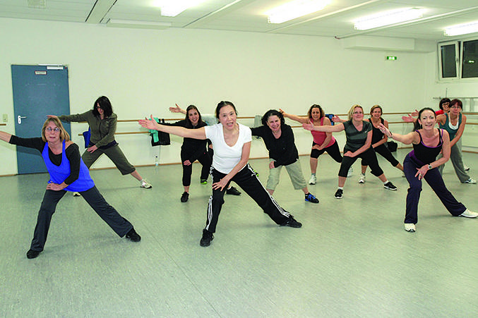 Gruppe von Frauen in sportlicher Kleidung, die synchron in einem Tanzstudio tanzen.